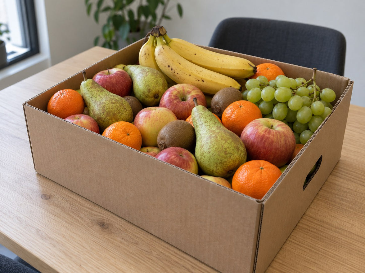Gefüllte Büro-Obstkiste mit verschiedenen frischen Früchten auf einem hellen Tisch.