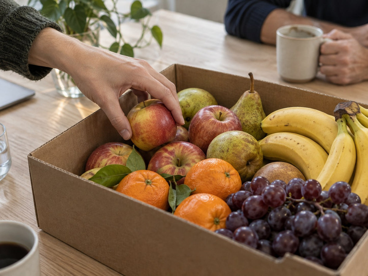 Eine Hand greift in der Büropause nach einem Apfel aus der Obstkiste.