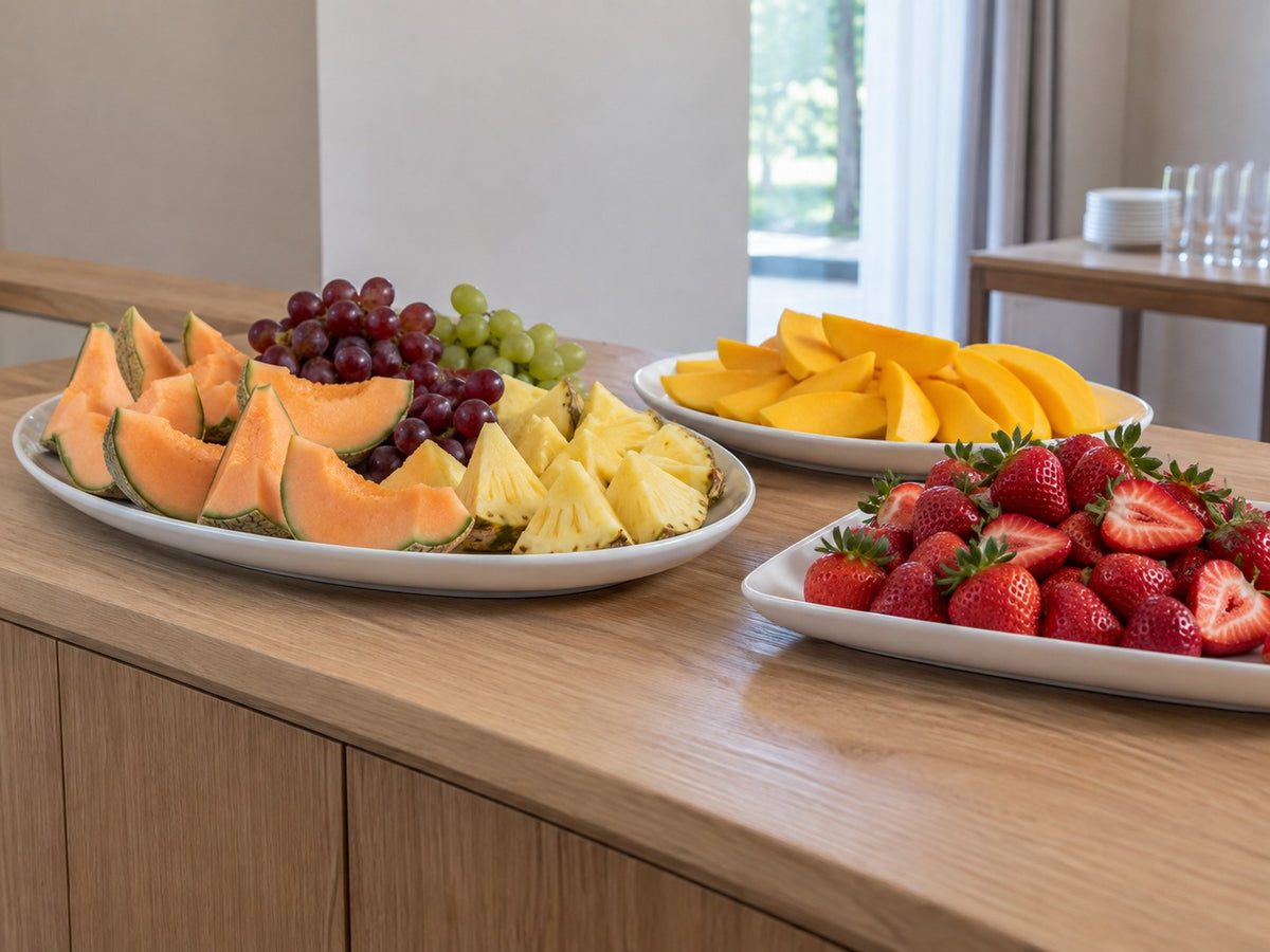 Obstbuffet mit Melone, Ananas, Mango, Erdbeeren und Trauben auf weißen Platten.