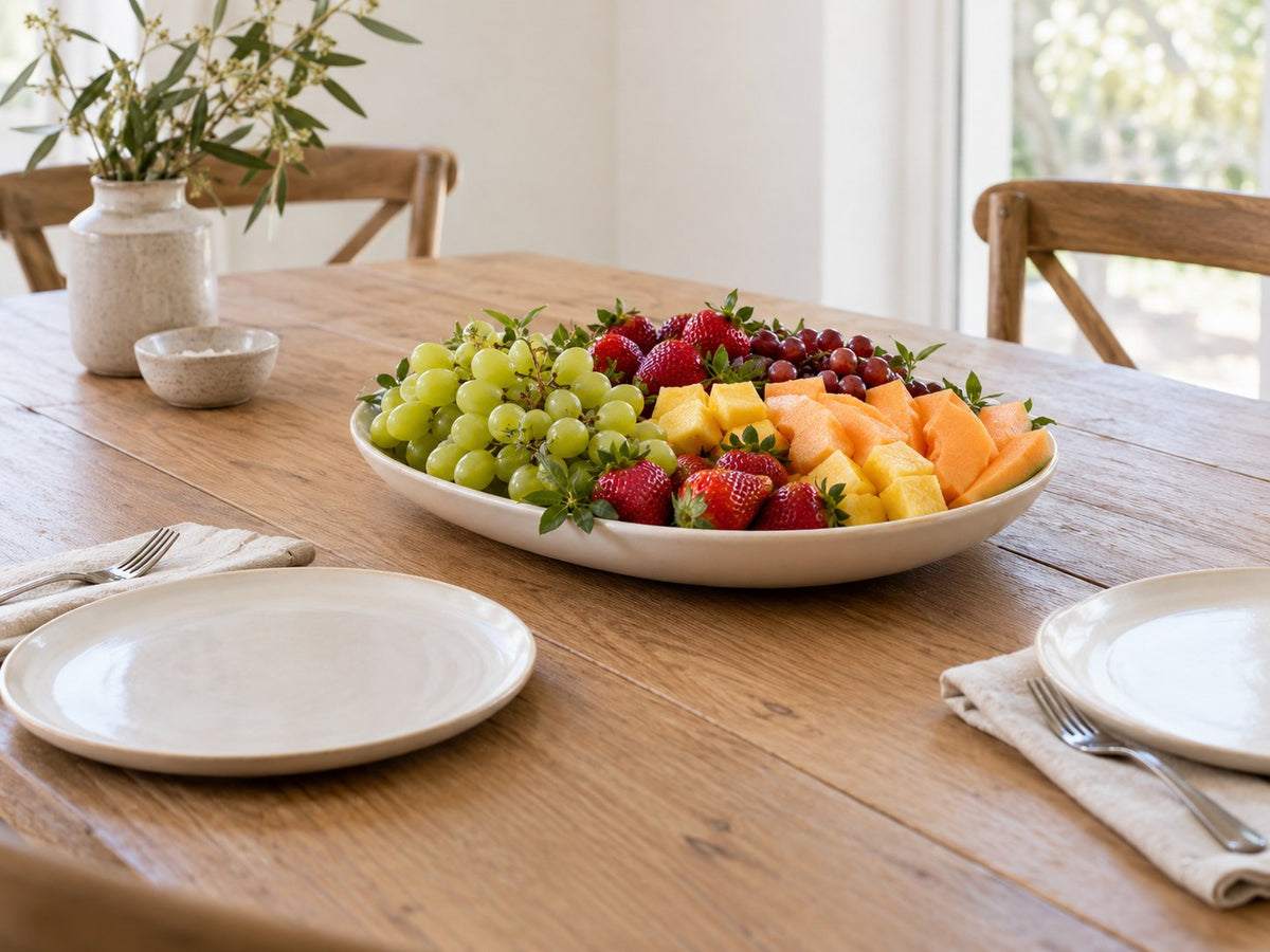 Obstplatte mit Melone, Ananas, Erdbeeren und Trauben auf einem gedeckten Holztisch.