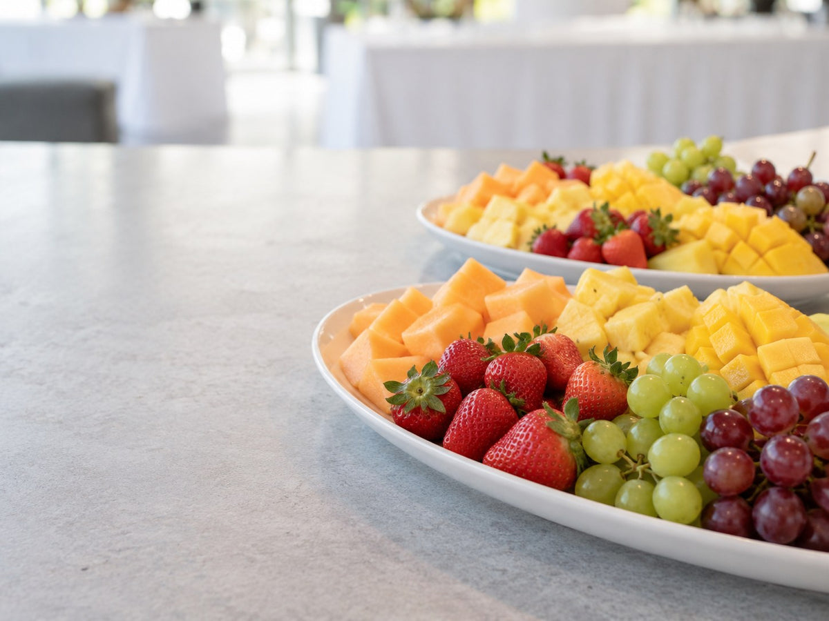 Zwei weiße Catering-Platten mit verschiedenem geschnittenem Obst.