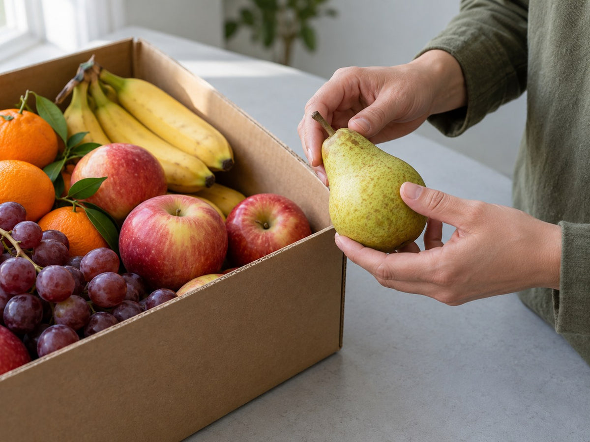 Hände prüfen eine Birne neben einer gefüllten Obstkiste.