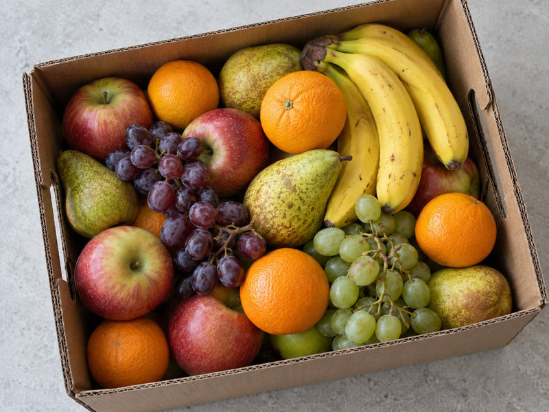 Dicht gefüllte Obstkiste mit Bananen, Äpfeln, Birnen und Trauben von oben.
