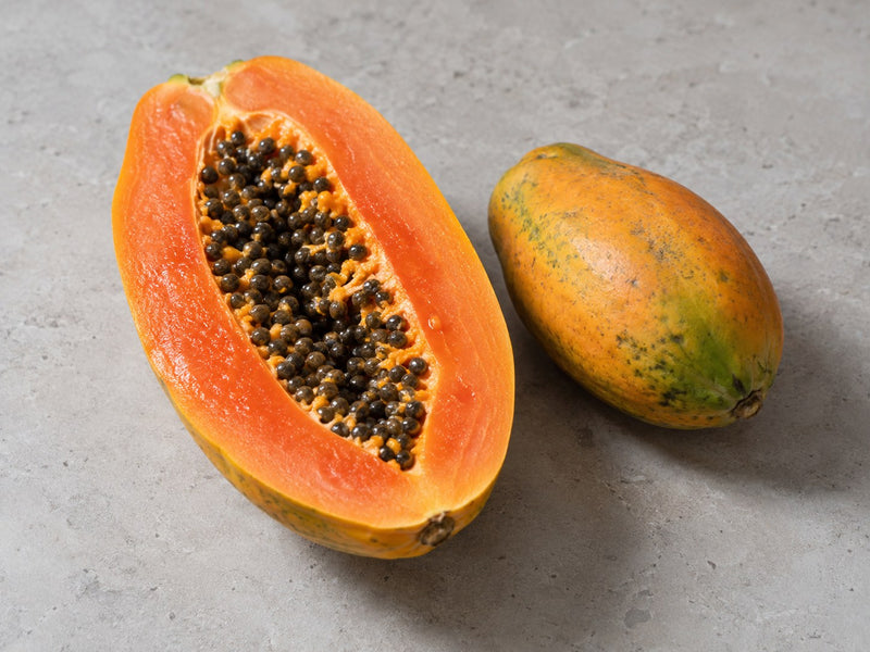 Ganze und halbierte Papaya mit orangefarbenem Fruchtfleisch und schwarzen Kernen.