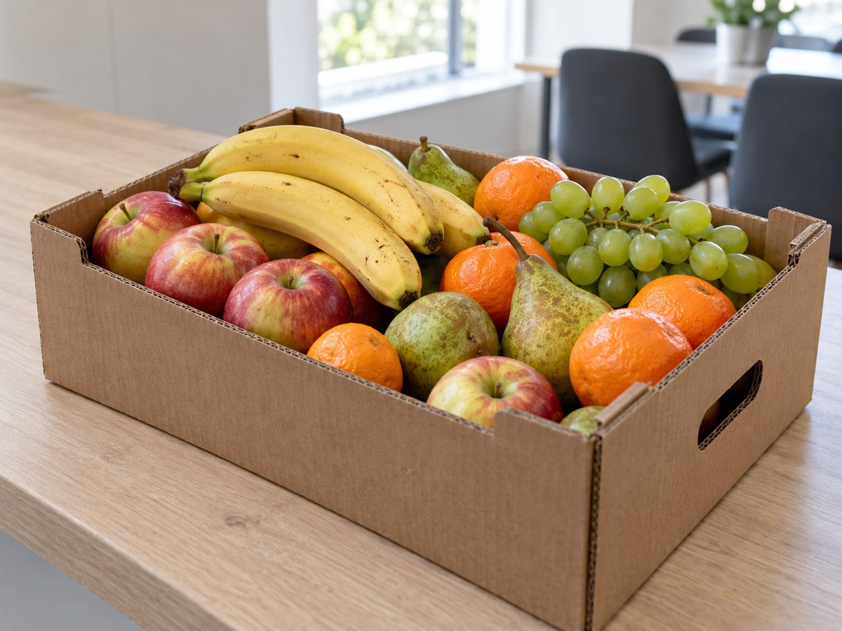 Obstkiste mit Bananen, Äpfeln, Birnen und weiteren Früchten in einer Büroküche.